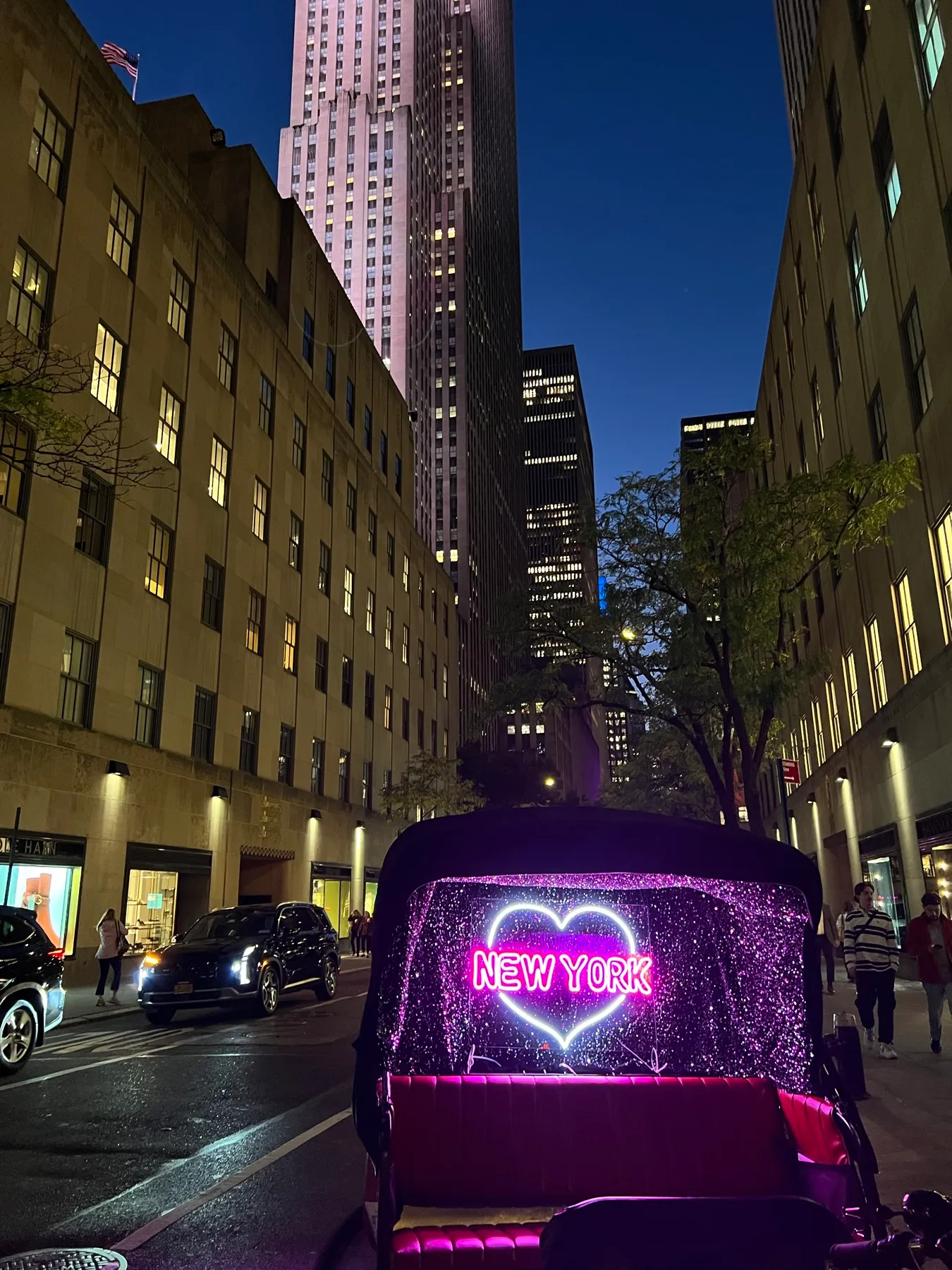 Rockefeller Center de noche con un bicitaxi con un corazón de neón